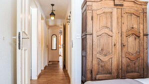 A hallway with wooden flooring, a large wardrobe, and a bed with a white bedspread. - Chesa Linaria by Interhome (Silvaplana-Surlej)