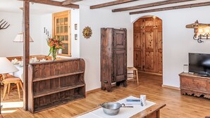 A rustic interior with exposed wooden beams, a wooden cabinet, a television on a wooden stand, and a dining area with a table and chairs. - Chesa Linaria by Interhome (Silvaplana-Surlej)