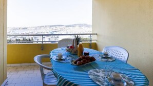 Un balcón con una mesa lista para dos personas, con vistas a un paisaje urbano.
