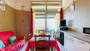 Una cocina compacta con una mesa de comedor, un sofá rojo y un televisor sobre un mueble.