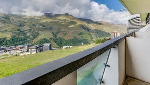 En balkon med udsigt over et bjerglandskab, bygninger og en klar himmel.