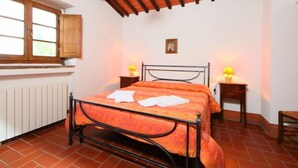 Un dormitorio con estructura de cama metálica, dos mesitas de noche con lámparas, un armario de madera y una ventana con vistas a zonas verdes.