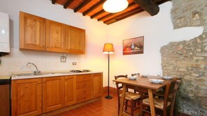 Una cocina con armarios de madera, piso de baldosas, una mesa de comedor con sillas, una lámpara y una pared de piedra.