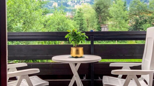 A balcony with a view of a mountainous landscape, a small round table with a potted plant, and two white chairs. - Rudis Appartements by Interhome (Bad Gastein)