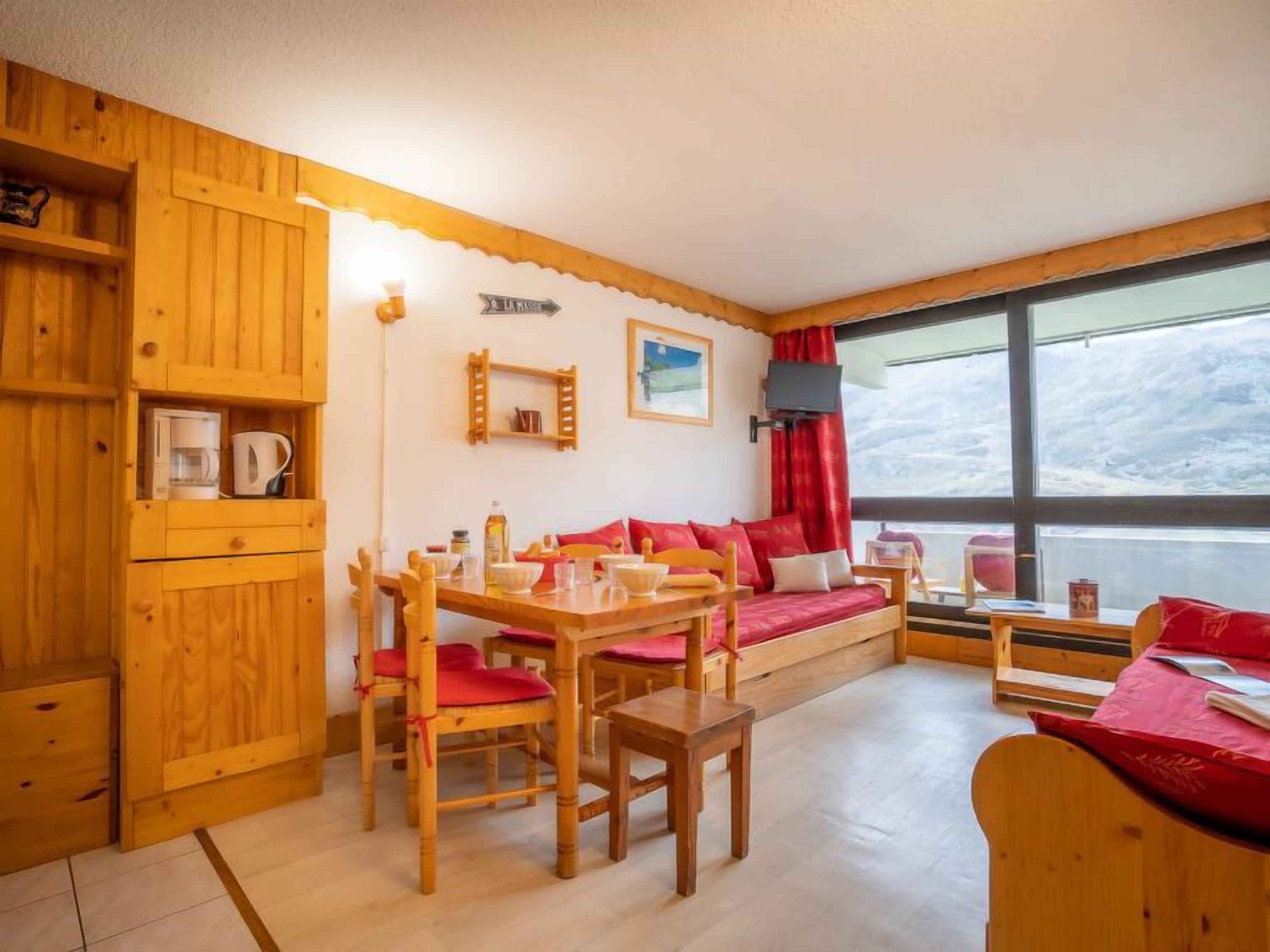 Um quarto aconchegante com móveis de madeira, uma mesa de jantar, um sofá e uma grande janela com vista para uma paisagem nevada.
