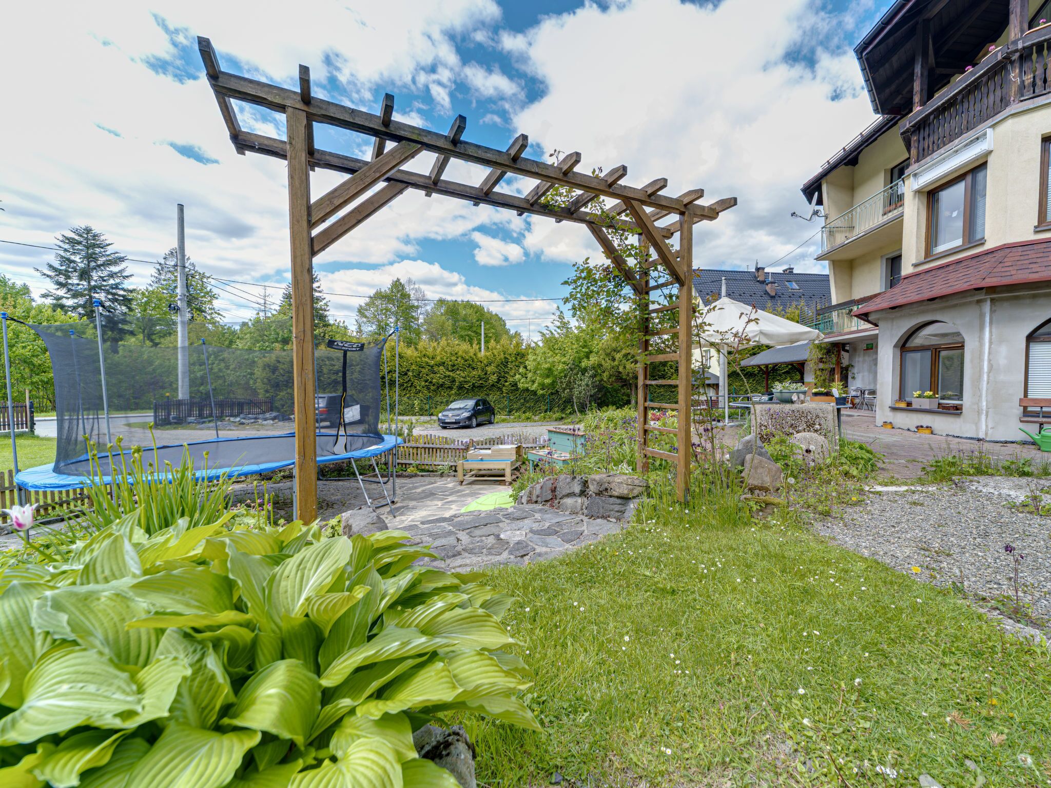 A garden with a wooden pergola, a trampoline, and a stone pathway.