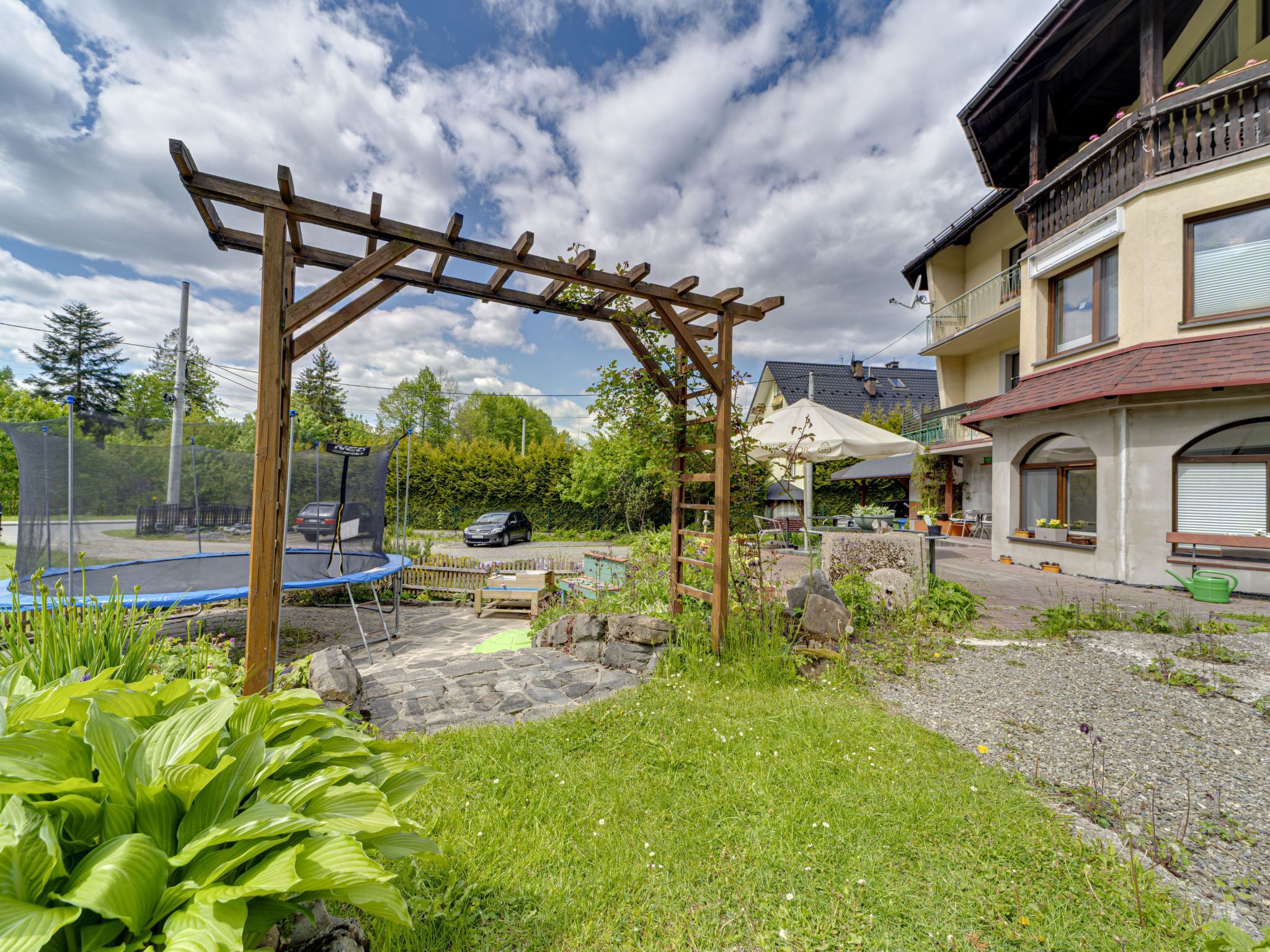 Ein Garten mit einer Holz-Pergola, einem Trampolin und einem gepflasterten Weg.