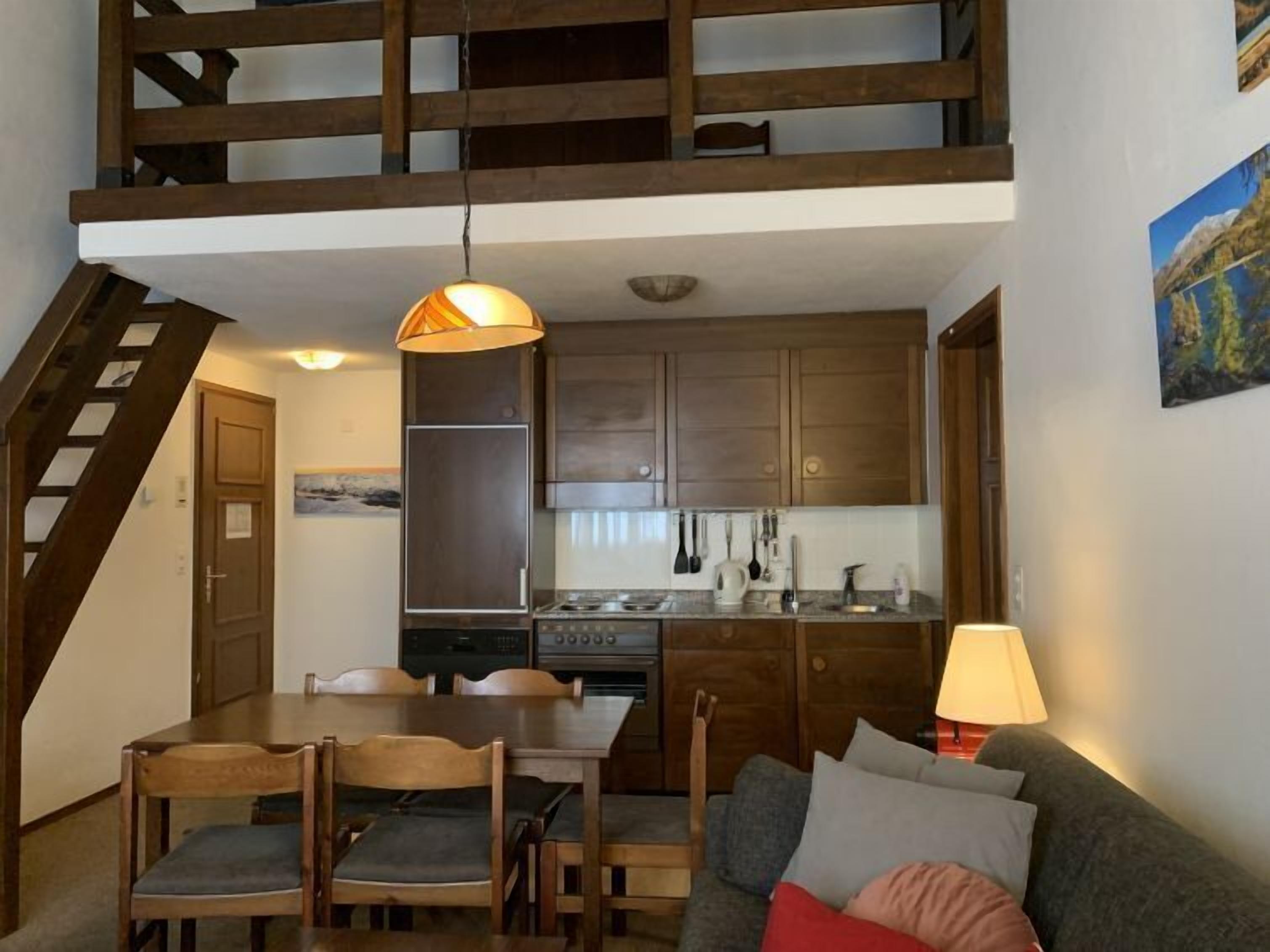Een moderne keuken met houten kastjes, een eettafel met stoelen, een trap en een schilderij aan de muur.