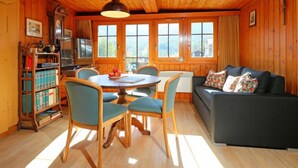 Ein gemütliches Blockhaus-Interieur mit Esstisch, Stühlen, einer Couch und einem Bücherregal.