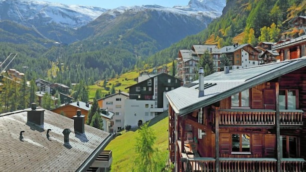 Ein Bergdorf mit traditionellen Holzhäusern, ein markanter Berggipfel im Hintergrund und ein klarer Himmel.