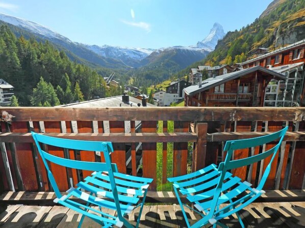 A balcony with two blue chairs overlooking a mountain view with buildings and a snow-capped peak. - Lauberhaus by Interhome (Zermatt)