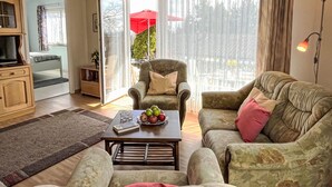 Una sala de estar acogedora con un sofá, un sillón y una mesa de centro, una televisión y una estantería.