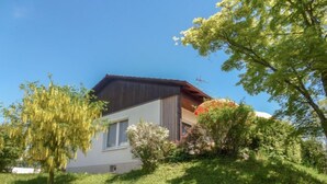 Una casa moderna con techo inclinado, rodeada de abundante vegetación y árboles.