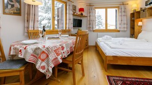 Ein gemütliches Zimmer mit einem Holzbett, einem Esstisch mit Stühlen und einem Fernseher an der Wand.