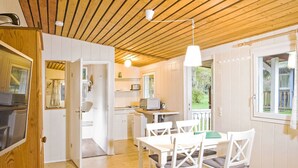 Una cocina moderna con armarios blancos, techo de madera y un comedor con sillas y mesa blancos.