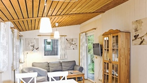 Una habitación acogedora con techo de madera, un sofá, una mesa de comedor con sillas, un aparador con puertas de cristal y un televisor montado en la pared.