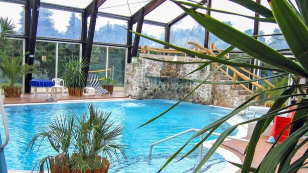 Una piscina interior con pared de piedra, un tobogán y sillones de descanso.