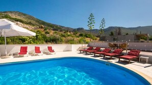 A swimming pool with red lounge chairs and a white umbrella, surrounded by a white wall and a view of mountains. - Apartment Orebić by Interhome (Orebić)