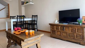 Una sala moderna con una mesa de comedor de madera, sillas, un televisor y un mueble.