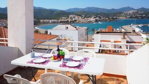 Una terraza con una mesa dispuesta para comer, con vistas a un pueblo costero y al mar.