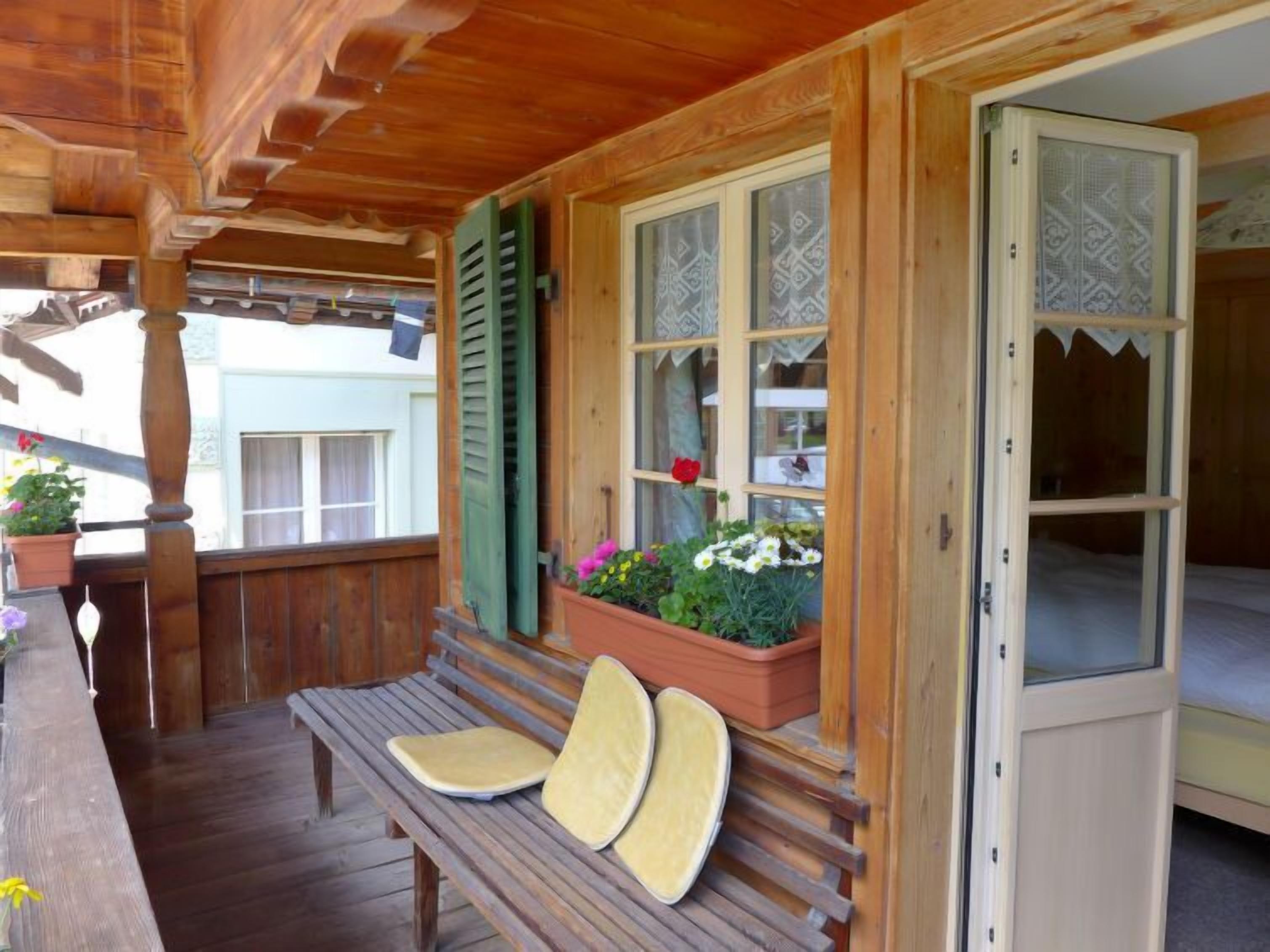 Un porche de madera con un banco, una ventana con contraventanas y una puerta.