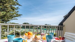 Ein Balkon mit Frühstücksangeboten, darunter Orangen, Brot und Erdbeeren, mit Blick auf einen Tennisplatz.