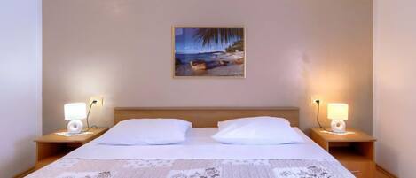 A hotel room with a large bed, two bedside tables with lamps, a painting on the wall, and a quilt on the bed.