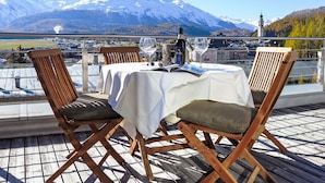 Une table dressée à l’extérieur, avec une vue sur les montagnes, des chaises en bois et une bouteille de vin.