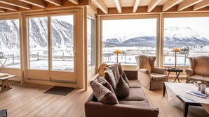 Un salon chaleureux avec une grande fenêtre donnant sur les montagnes, des poutres en bois au plafond et des sièges confortables.