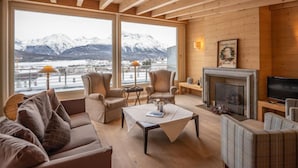 Un salon chaleureux avec une cheminée, de grandes fenêtres donnant sur des montagnes enneigées et des poutres en bois au plafond.