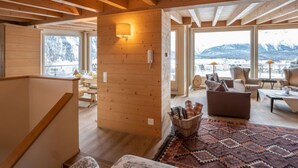 Un vaste espace de vie agrémenté de poutres en bois, une grande fenêtre offrant une vue sur les montagnes et un coin salon confortable.