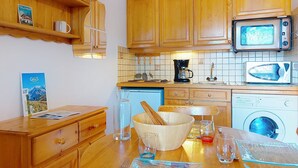 A compact kitchen with wooden cabinets, a microwave, a coffee maker, and a washing machine.
