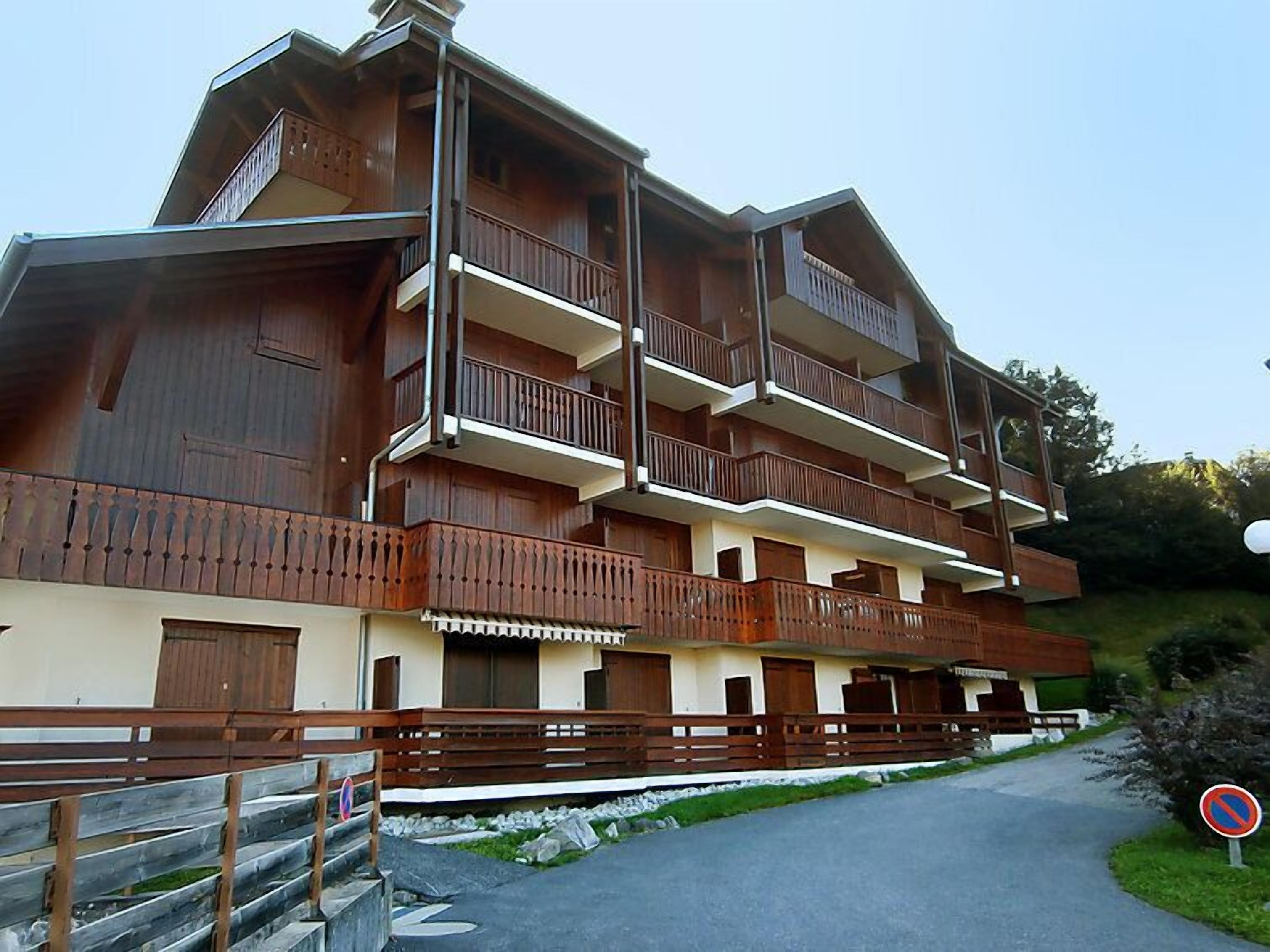 A multi-story wooden building with balconies, a stone pathway, and a no parking sign.