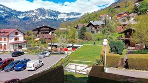 A mountain village with traditional wooden houses, a parking lot, and a view of snow-capped mountains.