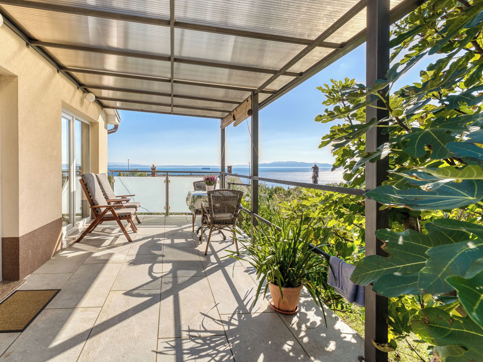 A covered balcony with two lounge chairs, a table, and a potted plant.