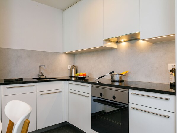 A modern kitchen with white cabinets, a black countertop, stainless steel appliances, and a built-in oven. - Residenza Chesa Margun 33-2 by Interhome (Silvaplana-Surlej)