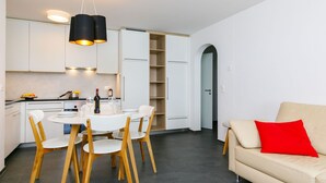 Une cuisine moderne avec des meubles blancs, une table à manger avec des chaises et un canapé agrémenté d’un coussin rouge.