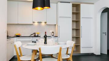 Une cuisine moderne avec des meubles blancs, une table à manger avec quatre chaises et une bouteille de vin posée sur le comptoir.
