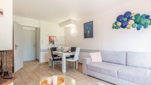 Een moderne woonkamer met een glazen salontafel, een grijze bank en een eethoek met een witte tafel en stoelen.