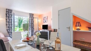 Een eetgedeelte met een tafel gedekt voor twee personen, een fles wijn en een televisie op de achtergrond.