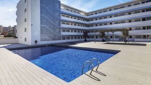 A rooftop pool area with a clear blue pool, a pergola, and a multi-story building with balconies. - Marcela by Interhome (St Antoni de Calonge)