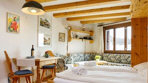 Ein gemütliches Zimmer mit einem hölzernen Bett, einem Schreibtisch mit Stuhl, einem Fenster mit Vorhängen und Wandbildern.