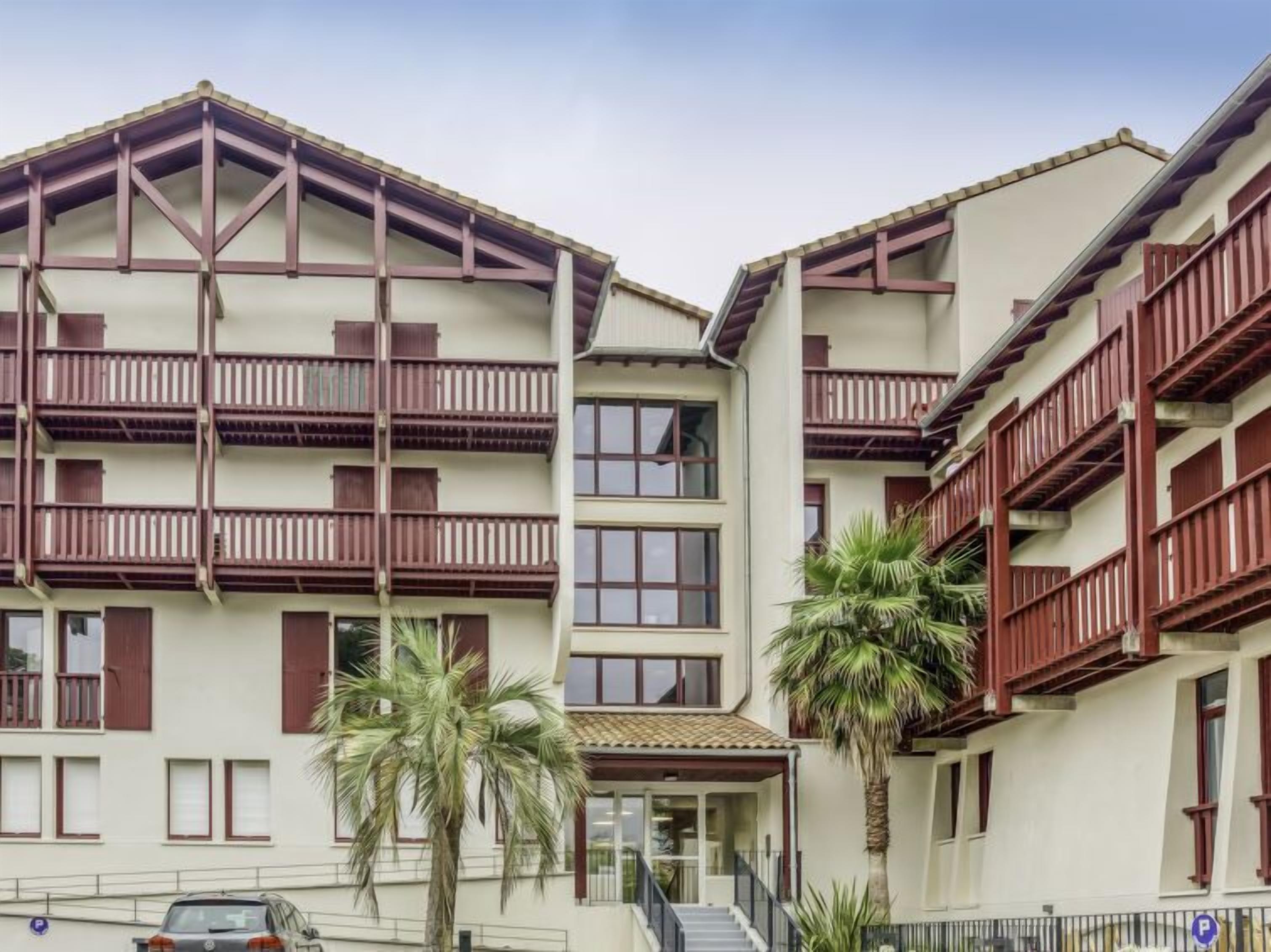 A multi-story hotel with balconies, a central entrance, and palm trees.