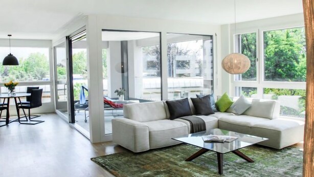 A modern living room with a sectional sofa, a glass coffee table, and a view of the outdoors through large windows. - LaVille B-2-3 by Interhome (Locarno)
