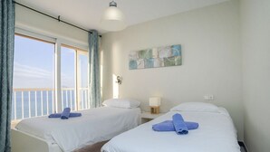A hotel room with two beds, a large window with curtains, a wall-mounted lamp, and a painting. - Les Roquetes by Interhome (Calpe/Calp)