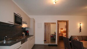 Een functionele keuken met een magnetron, koffiezetapparaat en een eethoek met een houten tafel en rode stoelen.
