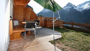 Een houten terras met een tafel en stoelen, met uitzicht op een bergachtig landschap.