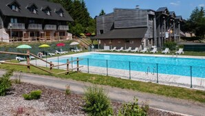 Ein Schwimmbecken mit Liegestühlen und Sonnenschirmen, umgeben von Gebäuden mit Balkonen.