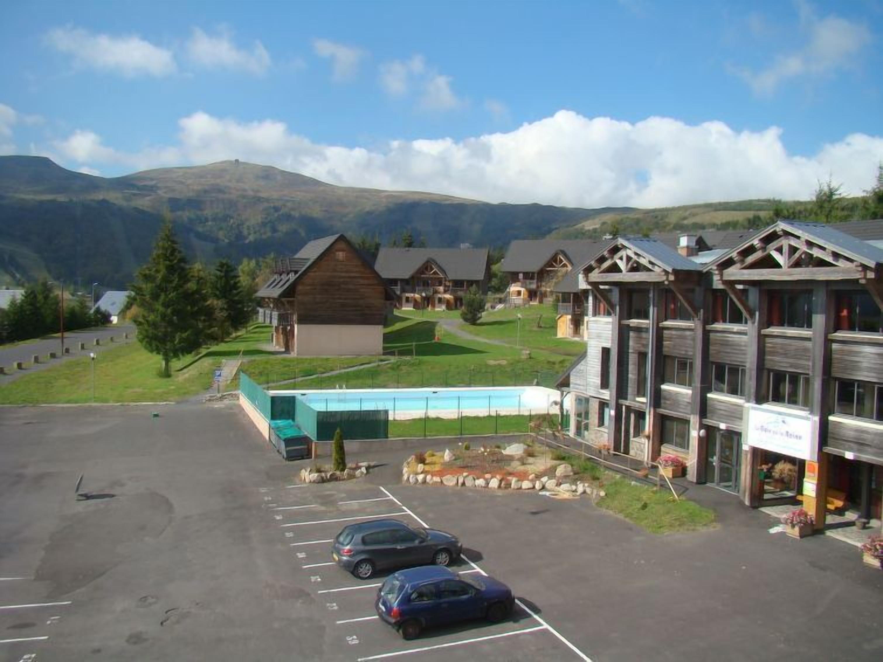 Ein Hotel mit mehreren Holzhäusern, einem Schwimmbad und einem Parkplatz mit zwei Autos.