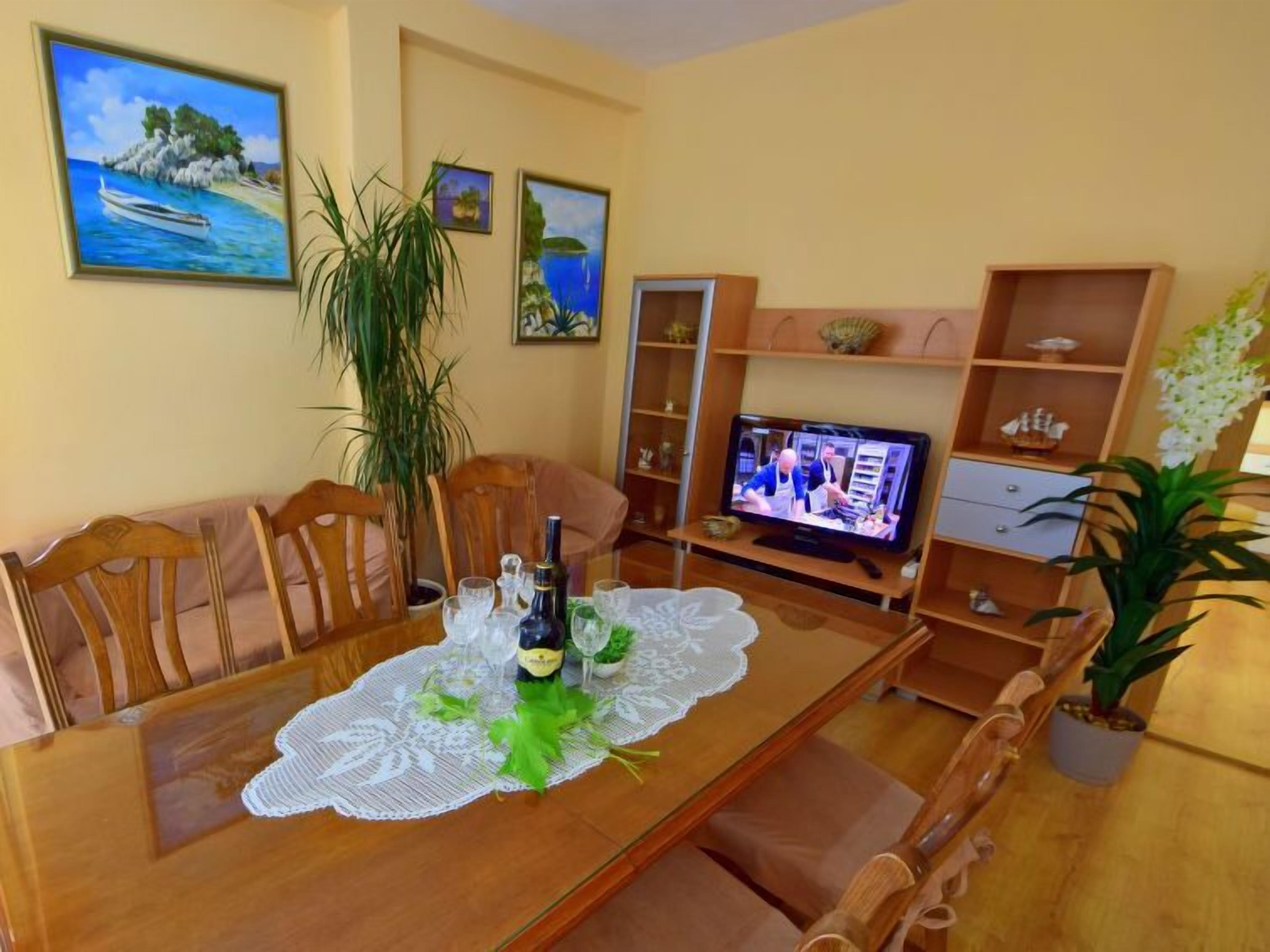 A dining area with a wooden table, chairs, a lace tablecloth, and a television displaying a cooking show.